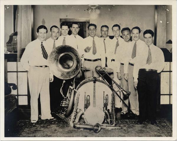10 musicians pose behind a tuba and drum kit in a black-and-white photo