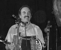 Mark sits with an accordion in his lap in front of two microphones preparing to play