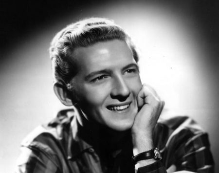 Under a spotlight, Jerry poses for a portrait. He wears a striped shirt and rests his chin on one arm.