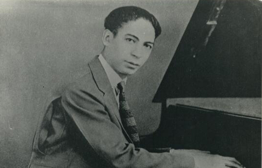 Jelly Roll looks at the camera while he plays the piano in a black-and-white picture