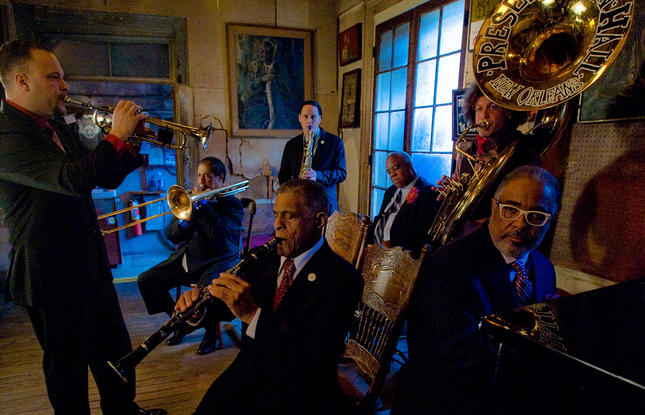 Jazz musicians in formal suits performing with various instruments inside the Preservation Hall in New Orleans, Louisiana.