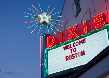 The brightly lit Dixie Theater marquee glows at dusk with a sign reading “Welcome to Ruston.”