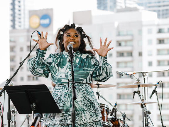 A performer smiles and gestures before a crowd.