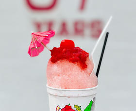 A pink and red snoball fills a cup, and is topped with a small drink umbrella.