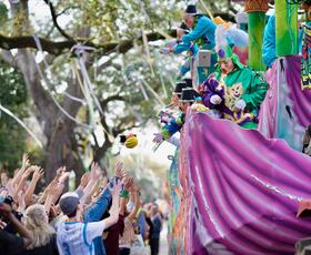 A crowed of parade goers reach out for Mardi Gras throws being tossed from a decorated and lively float.