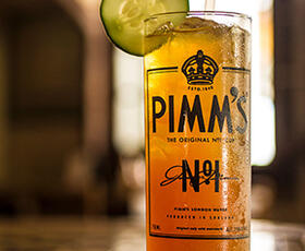A Pimm's Cup, featuring orange liquid, ice cubes and a cucumber slice garnish, sits on a table at Napoleon House in New Orleans.