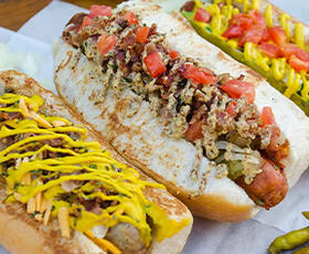 Three different hot dogs with thick buns and topped with ingredients like tomatoes, cheese and hot peppers sit on a table at Dat Dog in New Orleans.