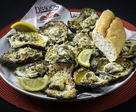 A plate of Drago's oysters are served with lemon wedges and a slice of bread.