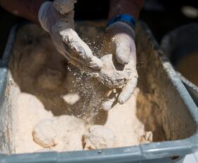 Gloved hands toss a boudin ball in seasoned flour.