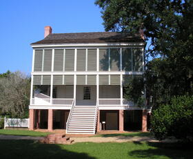 A view of the rear of the Oakley House at the Audubon Historic Site, with bright green window panes, surrounded by lush green trees and shrubs.
