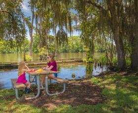 Mother and child eating at a picnic table under moss-draped oaks by the water at Fairview-Riverside State Park.