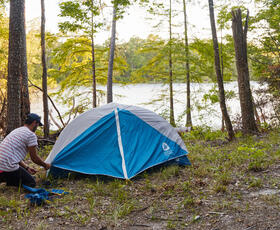 Camper setting up a blue tent in a forest clearing overlooking the lake at South Toledo Bend State Park.
