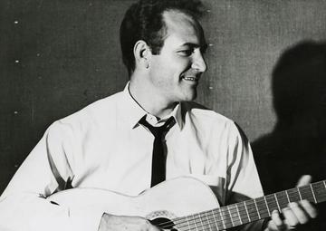 Fred Carter Jr. strums a guitar and smiles off to the viewer's right
