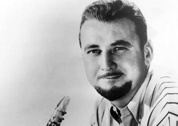 Pete lays on his stomach, propped up and holding his clarinet. he wears a white-striped shirt