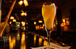 A sparkling French 75 cocktail in a champagne flute, glowing under warm bar lights at Arnaud’s Restaurant.