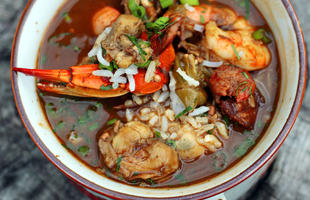 A red bowl piled high with seafood gumbo in a rich, tomato broth, with shrimp, crawfish and other seafood.
